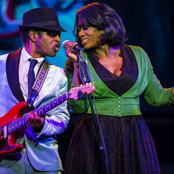Ike seitlich im Anzug mit roter Gitarre und Tina in grüner Jacke gemeinsam singend
