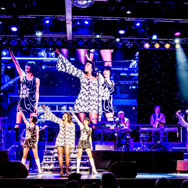 4 Sängerinnen und Musiker im 70ziger Jahre Outfit gemeinsam auf der Bühne